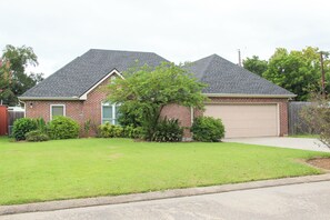 A two-story house with a garage, surrounded by a well-maintained lawn and various shrubs. - Aryn Ridge House / 3BR / Near Casinos & Interstate (Lake Charles)