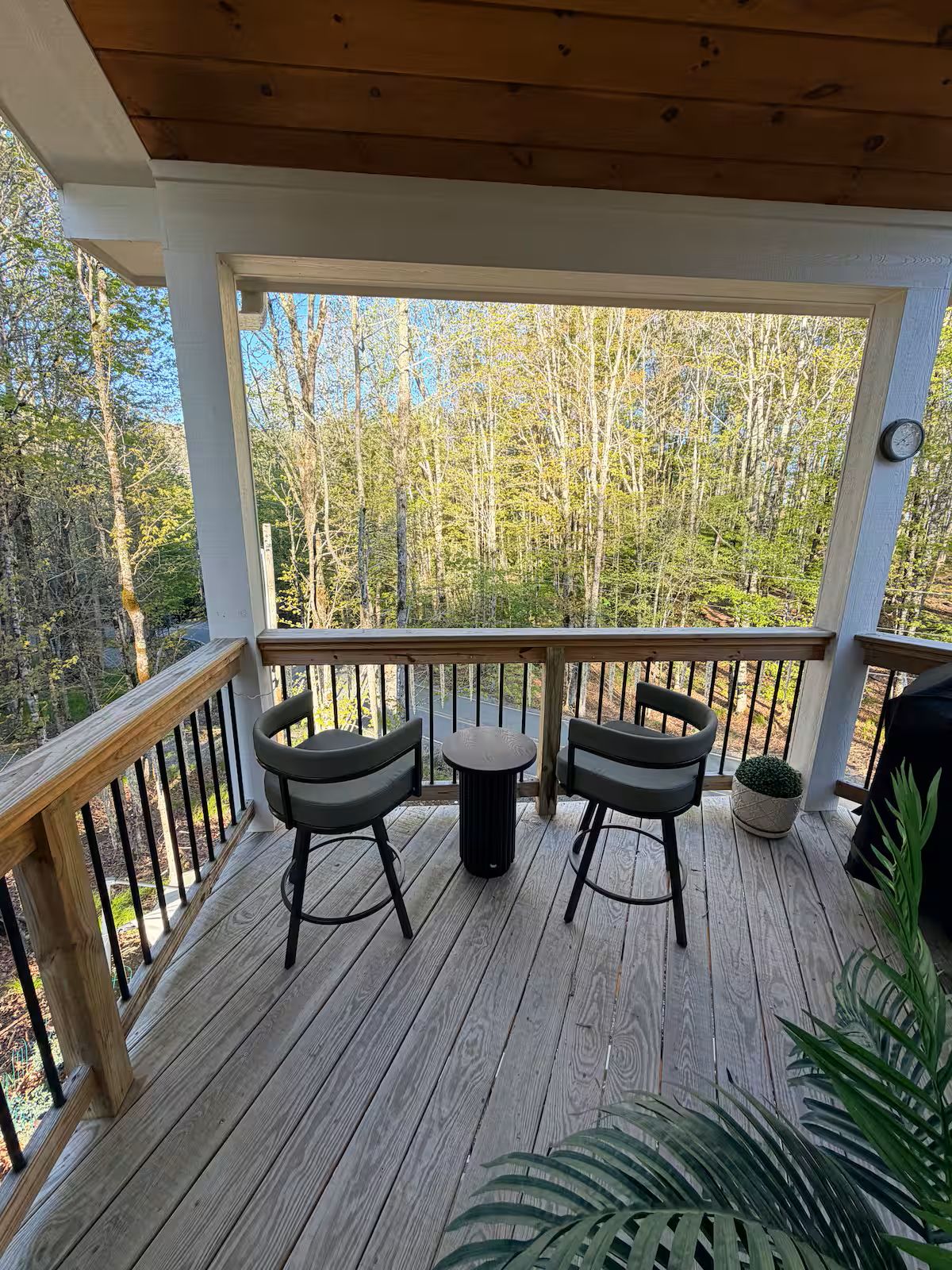 Une terrasse en bois avec deux chaises et une table, entourée d’une rambarde, donnant sur une zone boisée.