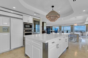 A modern kitchen with white cabinetry, stainless steel appliances, and a large island with a built-in sink. - Stunning Beachfront Penthouse | Luxury Living & Gulf Views (Naples)