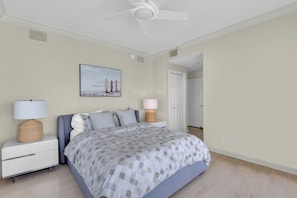 Ein Schlafzimmer mit einem Bett, zwei Nachttischlampen, einem Deckenventilator, einem Bild an der Wand und einer weißen Tür.