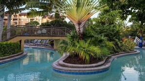 A pool area with a palm tree, lounge chairs, and a building in the background.