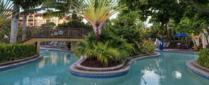 A pool area with a palm tree, lounge chairs, and a building in the background.
