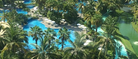 Un complexe hôtelier doté de plusieurs piscines, entouré de palmiers et d’une végétation luxuriante.