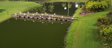 Ein Golfplatz bei Nacht mit gut beleuchteten Bereichen, einem Teich und einer Steinbrücke.