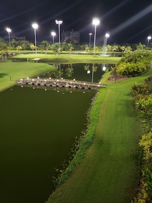 Un parcours de golf illuminé la nuit, avec des zones bien éclairées, un étang et un pont en pierre.