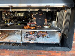 Une personne prépare des fruits de mer sur un barbecue extérieur doté d’une base en briques et d’une grille en métal.