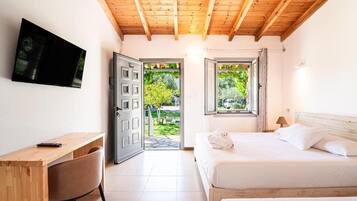 A bedroom with a bed, a desk, a chair, a TV, and two windows.