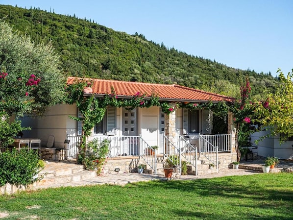 Una casa con techo de tejas rojas, una escalera de piedra y un jardín con plantas en macetas.