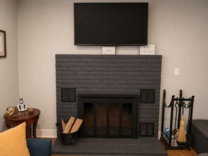 Una sala de estar con chimenea, un televisor de pantalla plana montado encima y una mesita con adornos.
