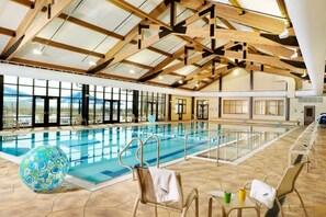 An indoor swimming pool with clear views of the outdoors, wooden beams on the ceiling, and lounge chairs with towels. - Pecker’s Nest  Cozy Cottage in Galena Territory (Galena)