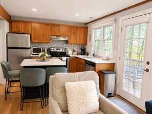 A modern kitchen with wooden cabinets, stainless steel appliances, and a dining area with a bar stool. - Pecker’s Nest  Cozy Cottage in Galena Territory (Galena)