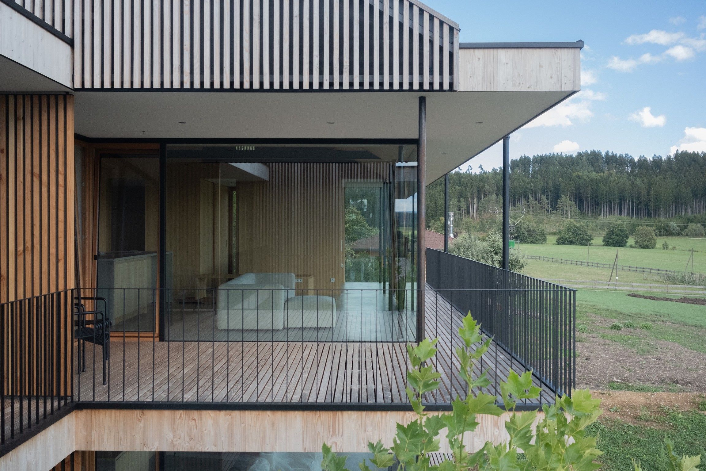 Ein modernes Gebäude mit Balkon, großen Fenstern und Blick auf einen Wald.