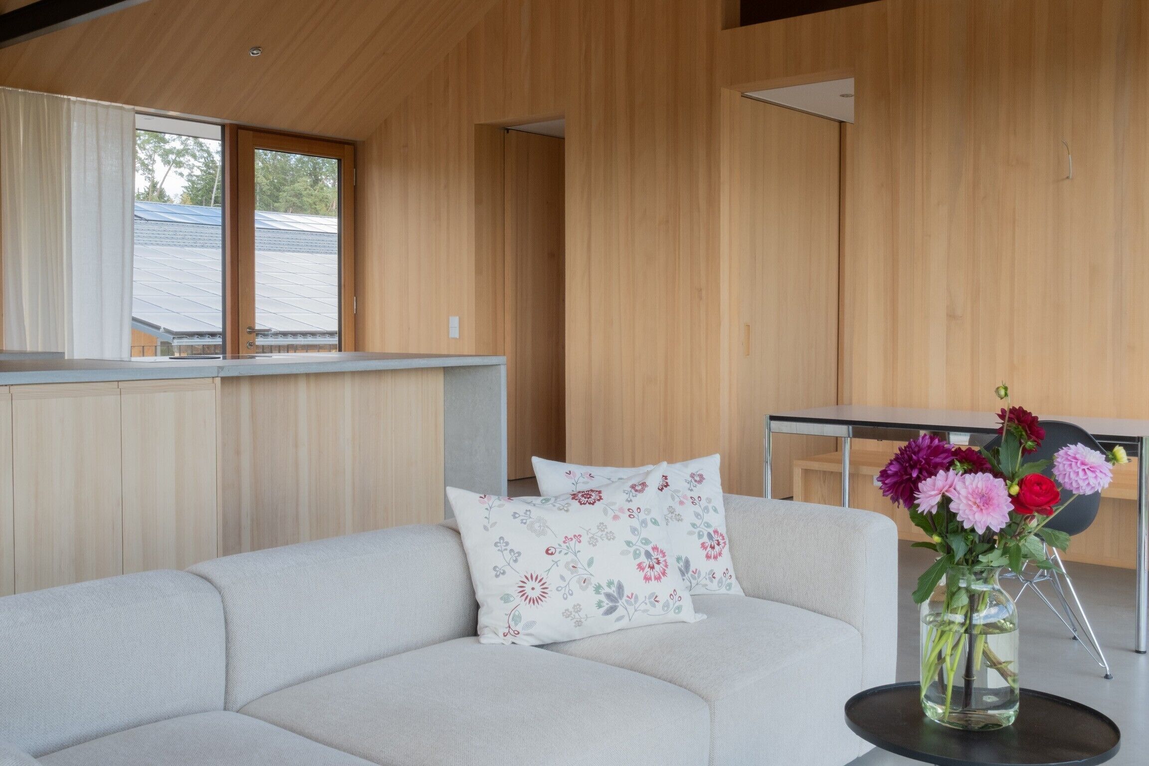 Een moderne woonkamer met een hoekbank, een houten wand en een raam met uitzicht op een dak.