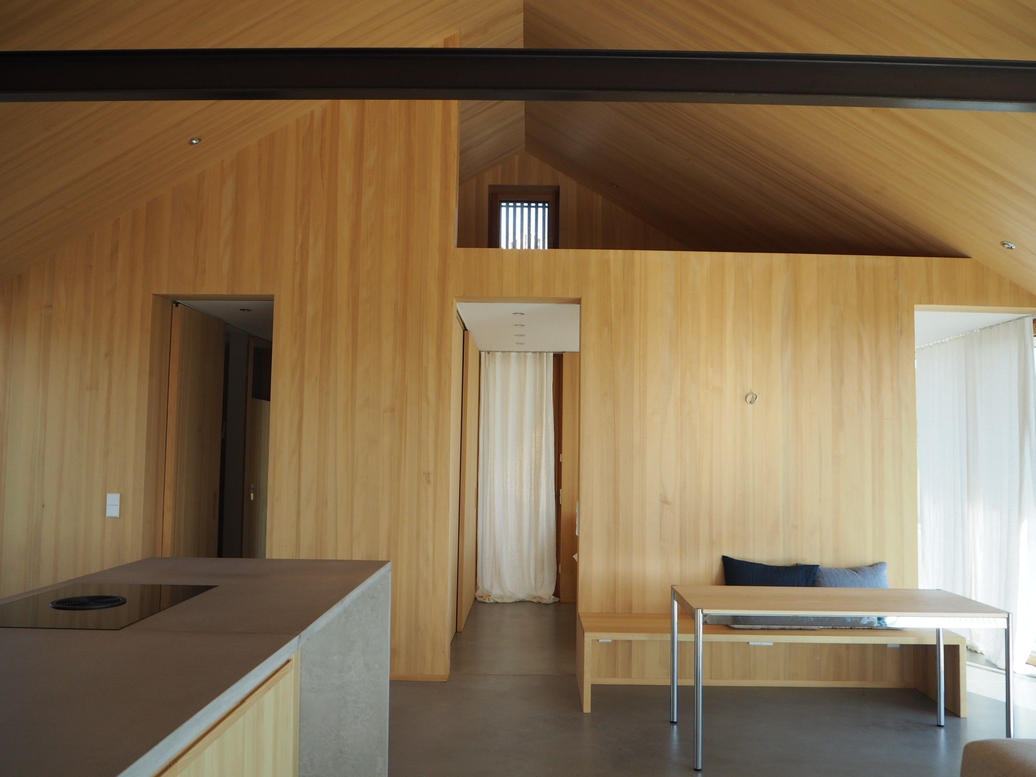 Ein modernes Interieur mit Holzvertäfelung, einer Küchenzeile, einem Essbereich und einem kleinen Fenster.
