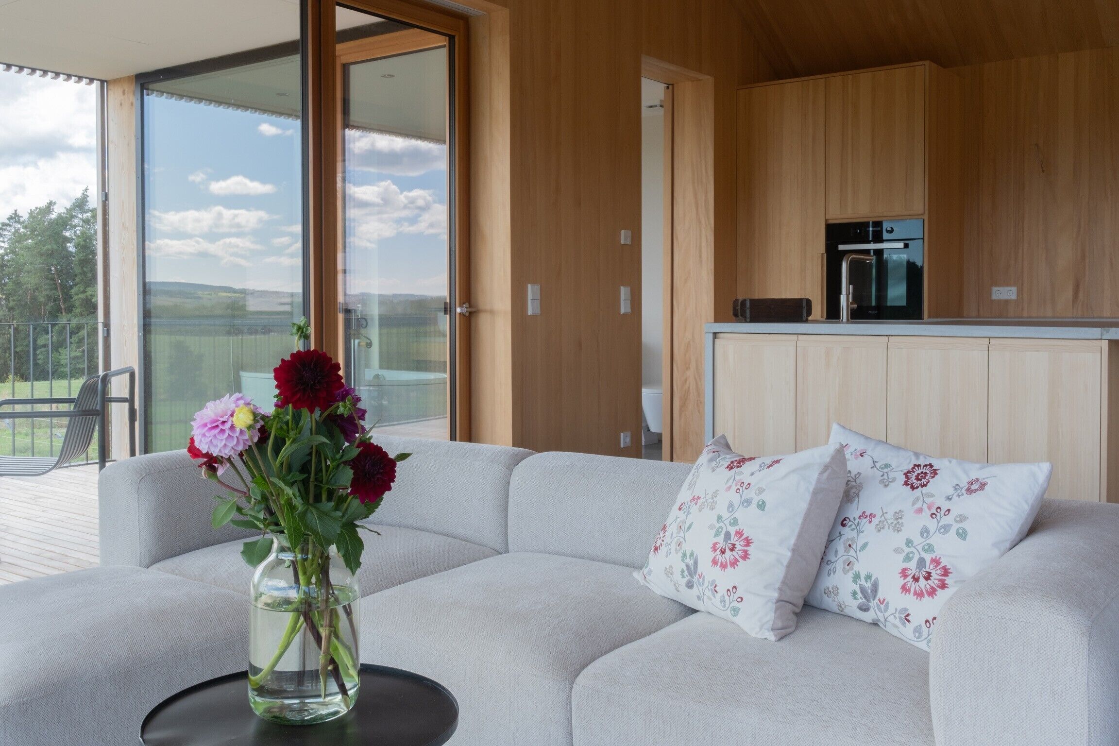 Een moderne woonkamer met een bank, een bloevas en uitzicht op het buiten.