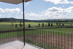 Un balcó amb vistes a un paisatge verd, incloent camps i una zona boscosa.