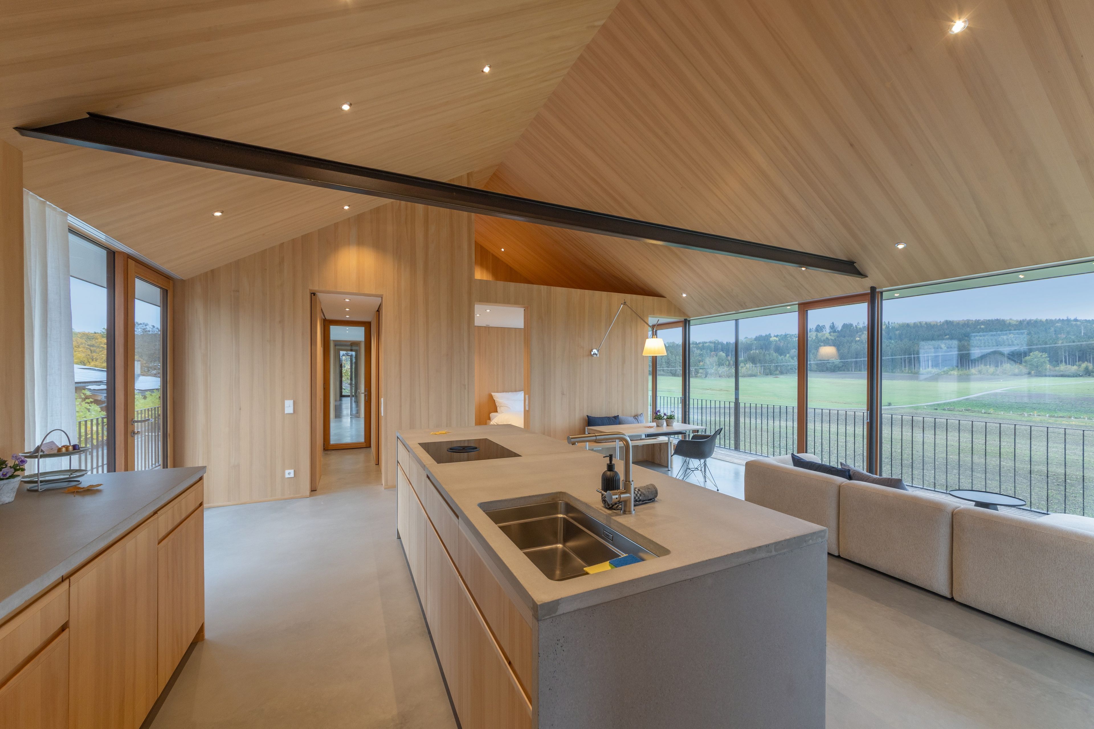 Eine moderne Küche mit einer großen Kochinsel, Holzschränken und Blick auf eine grüne Landschaft durch große Fenster.