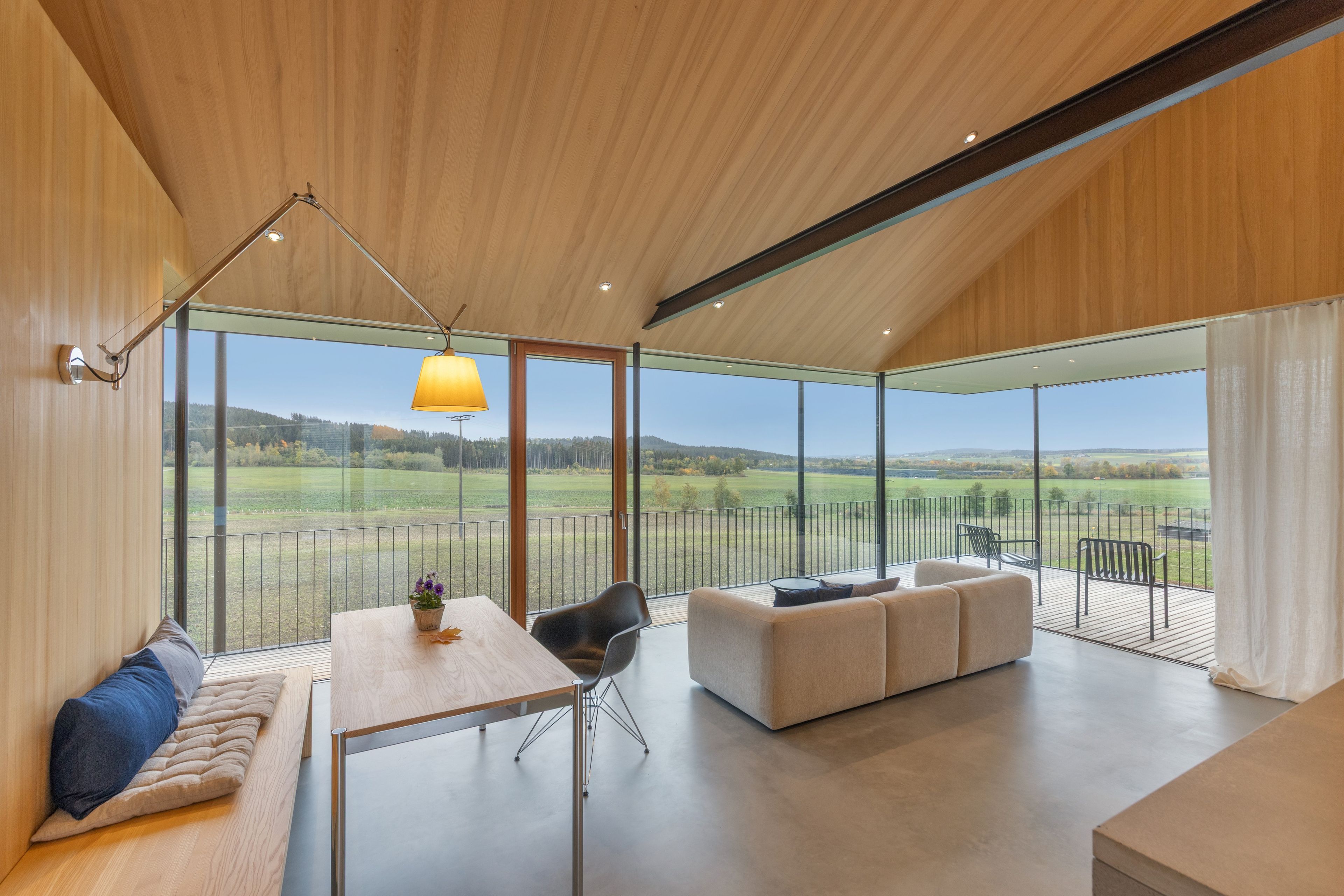 A modern interior with a dining area, seating, and a large glass window offering a view of the countryside.