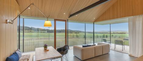A modern interior with a dining area, seating, and a large glass window offering a view of the countryside.
