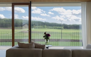 A room with a large window overlooking a golf course, a sofa, and a vase with flowers. - Quiet Apartment with Panoramic Countryside Views, Two Balconies, and Parking (Bad Dürrheim)
