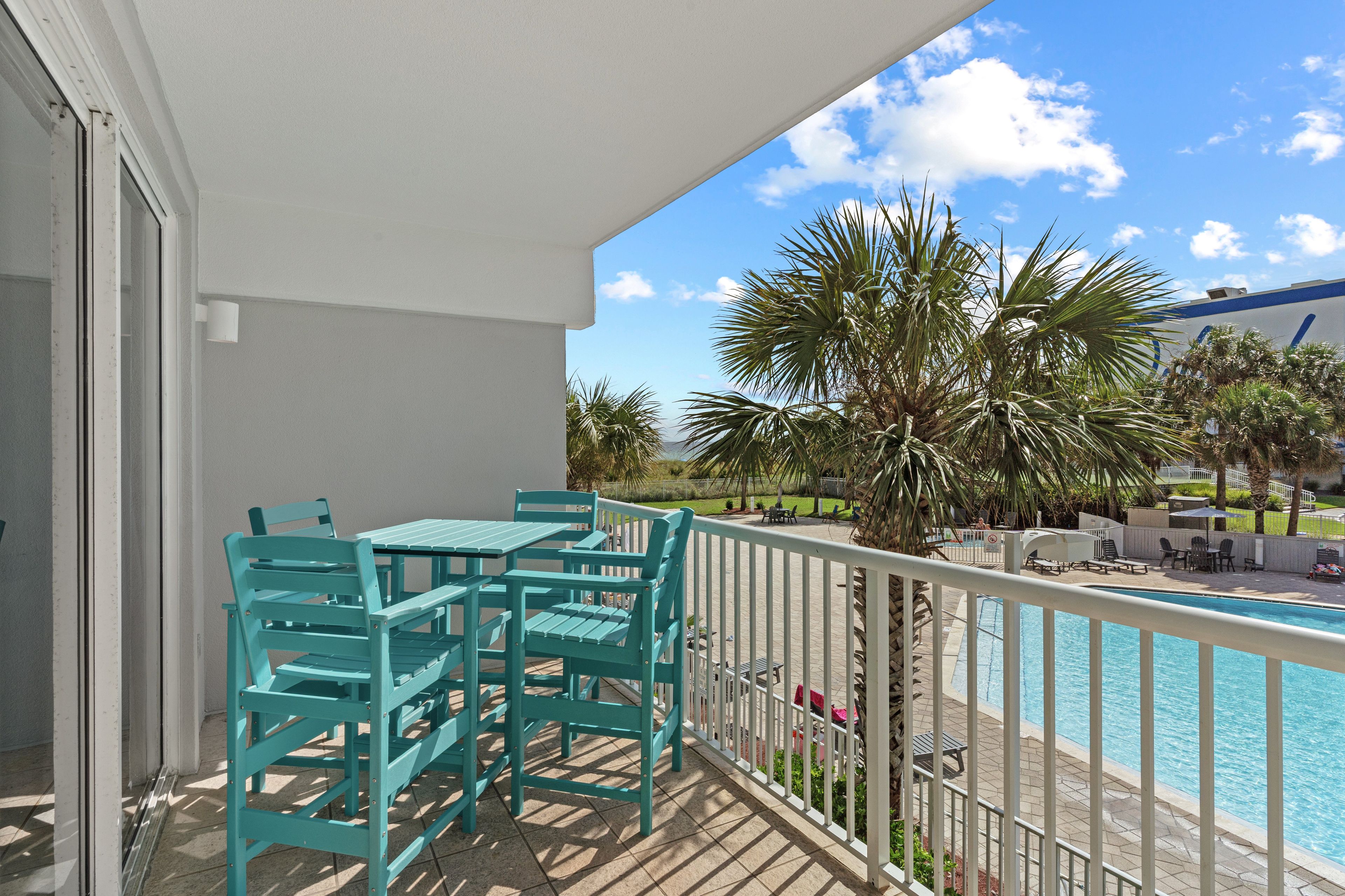A balcony with turquoise chairs and a pool.