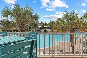 A poolside area with a view of a building in the background, surrounded by palm trees. - Destin West Gulfside 205 ~ Ocean Views ~ Beach Service Included (Fort Walton Beach)