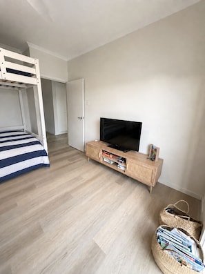 Ein Schlafzimmer mit einem Etagenbett, einem Fernseher auf einem Holzschrank und einem Korbwäscher mit Zeitschriften.