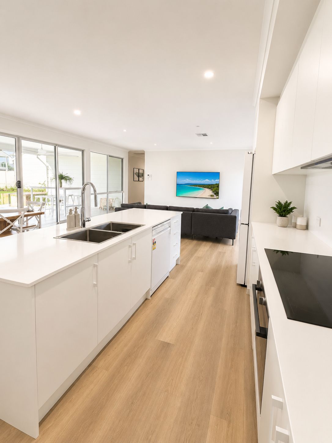 Una cocina moderna con armarios blancos, una isla central con pileta y un comedor con vista al exterior.