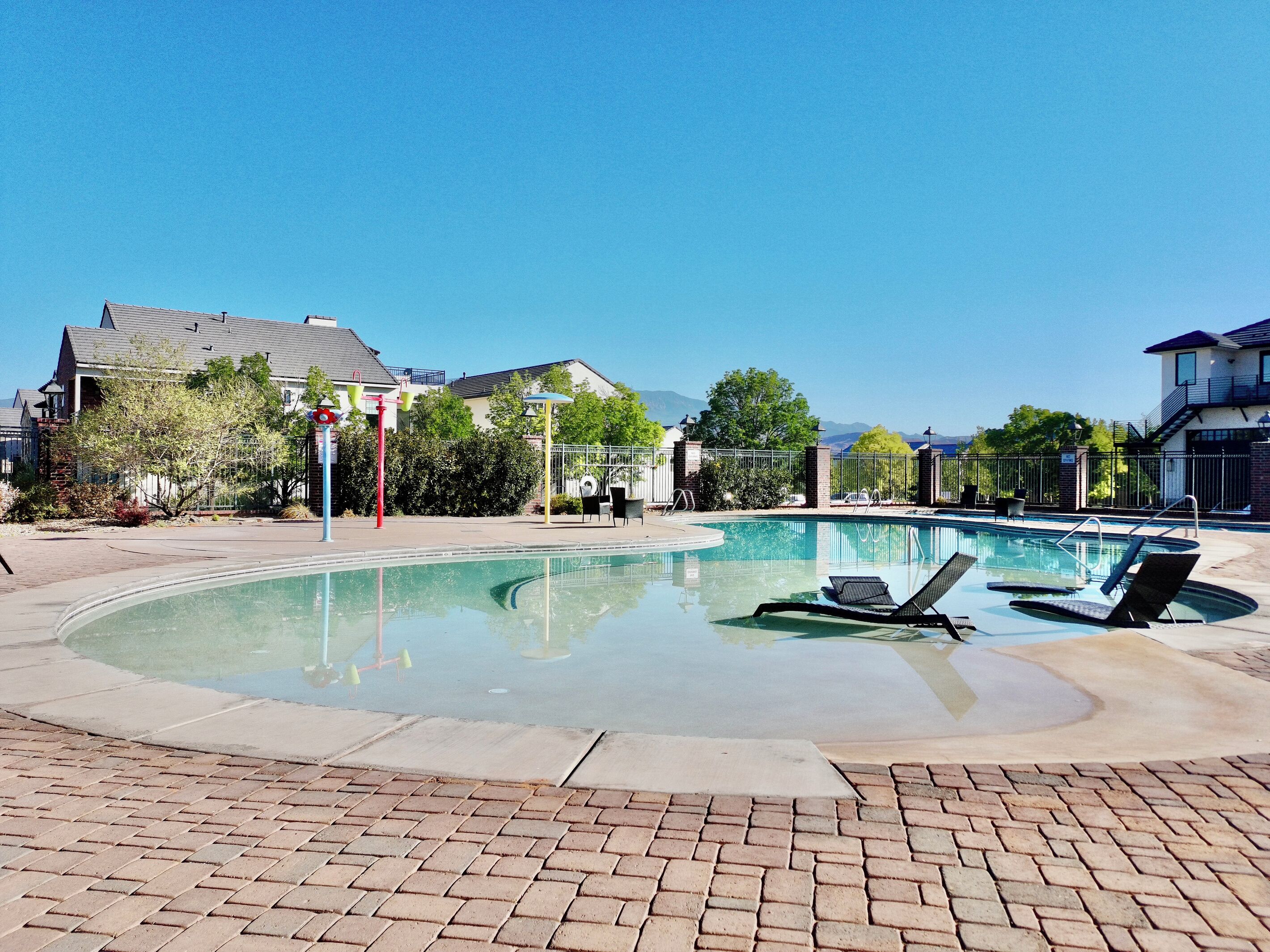 A swimming pool with lounge chairs, a brick pathway, and houses in the background.