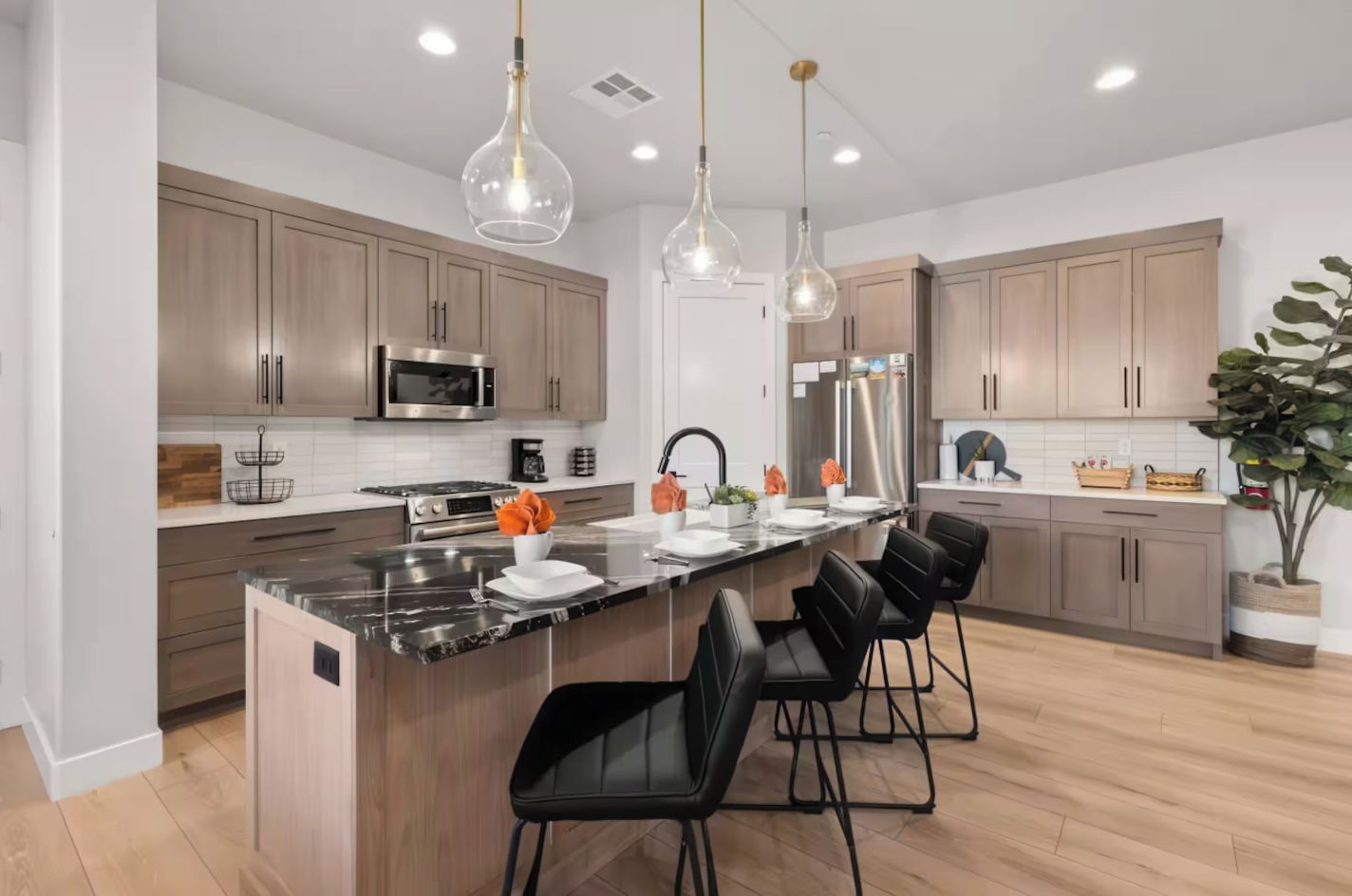 A modern kitchen with a central island, stainless steel appliances, and black bar stools.