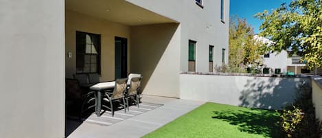 Un bâtiment moderne doté d’un patio comprenant une table et des chaises, le tout entouré d’une pelouse bien entretenue.