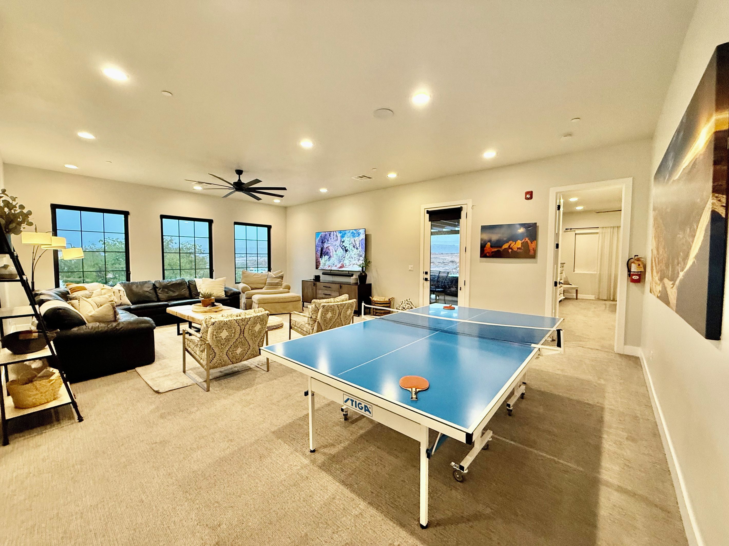 A spacious living area with a ping pong table, comfortable seating, a television, and large windows.