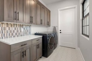A laundry room with a washing machine, cabinets, and a tiled backsplash. - Desert Sands Basecamp | Hot Tub | Pool | Fire Pit (Hurricane)