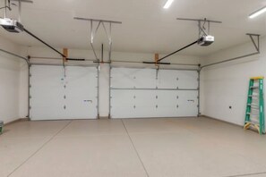 A spacious garage with two large garage doors, overhead lighting, and a green ladder. - Desert Sands Basecamp | Hot Tub | Pool | Fire Pit (Hurricane)