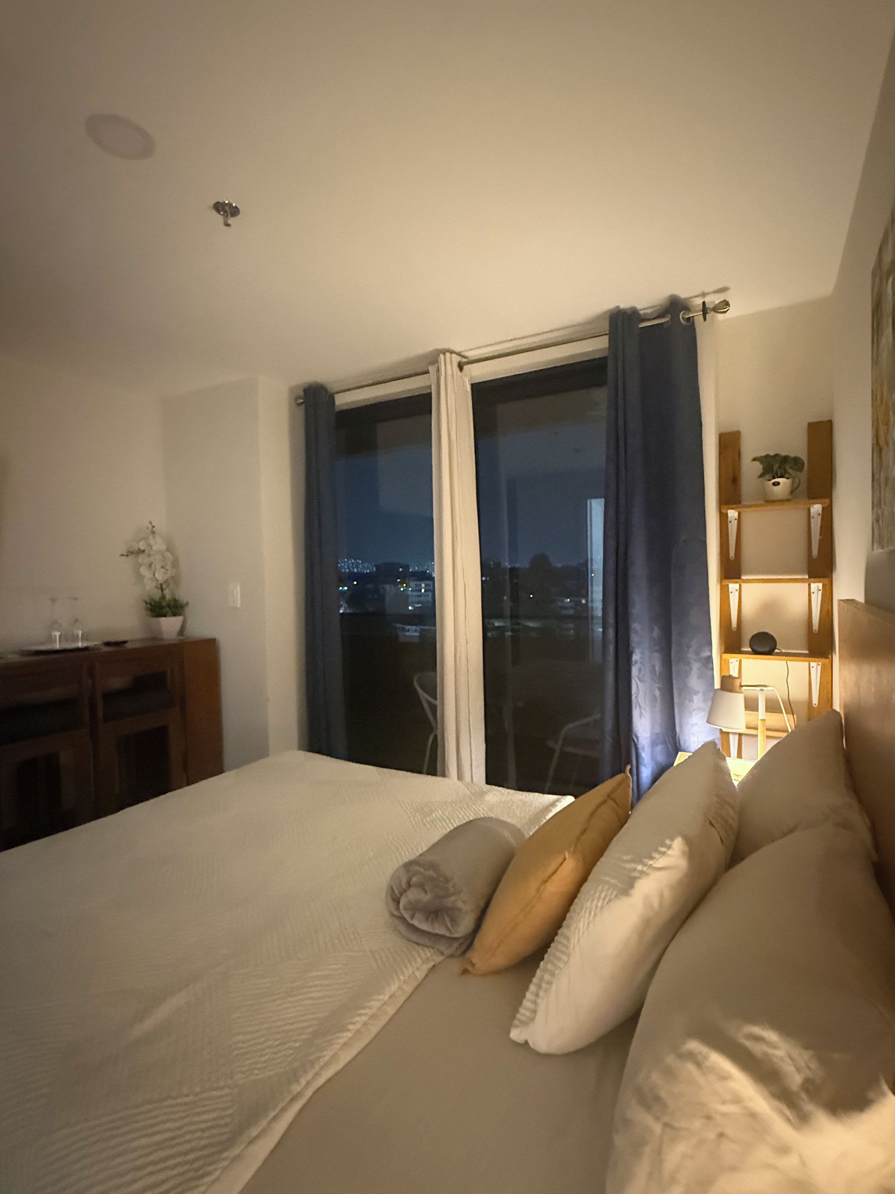 Ein Hotelzimmer mit Bett, Schreibtisch, Stuhl, einem fenster mit Vorhängen und Blick auf die beleuchtete Stadt.