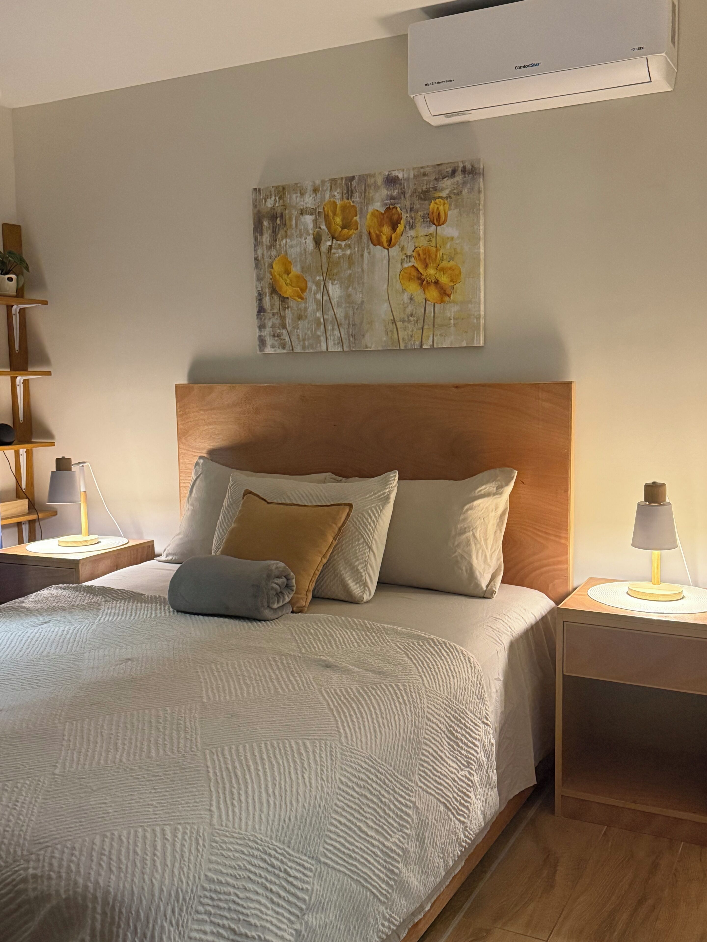 A bedroom with a bed, a headboard, a nightstand, a lamp, and a wall-mounted air conditioner.