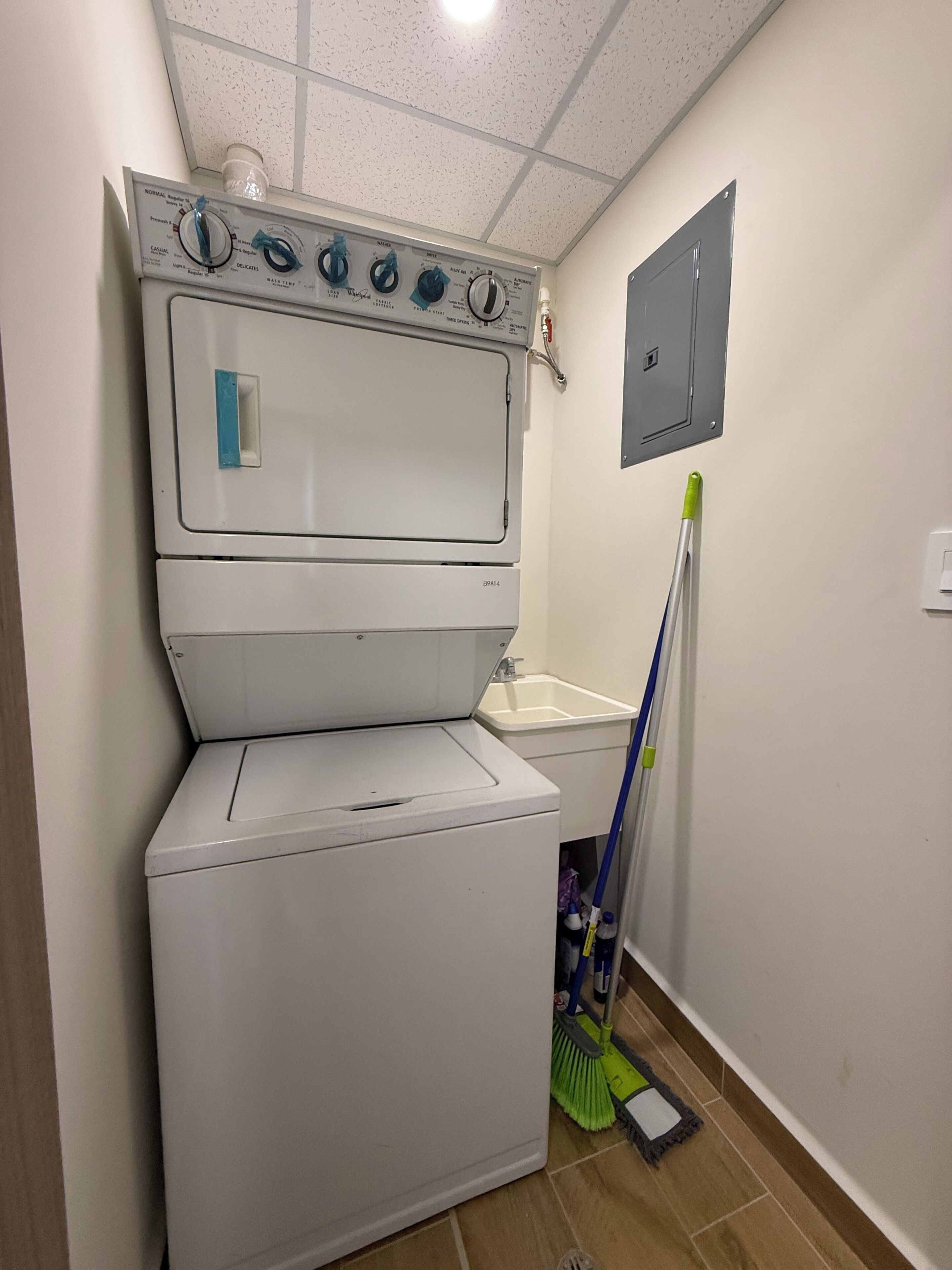 Een wasserette met een gestapelde wasmachine en droger, een dweil en een kast.