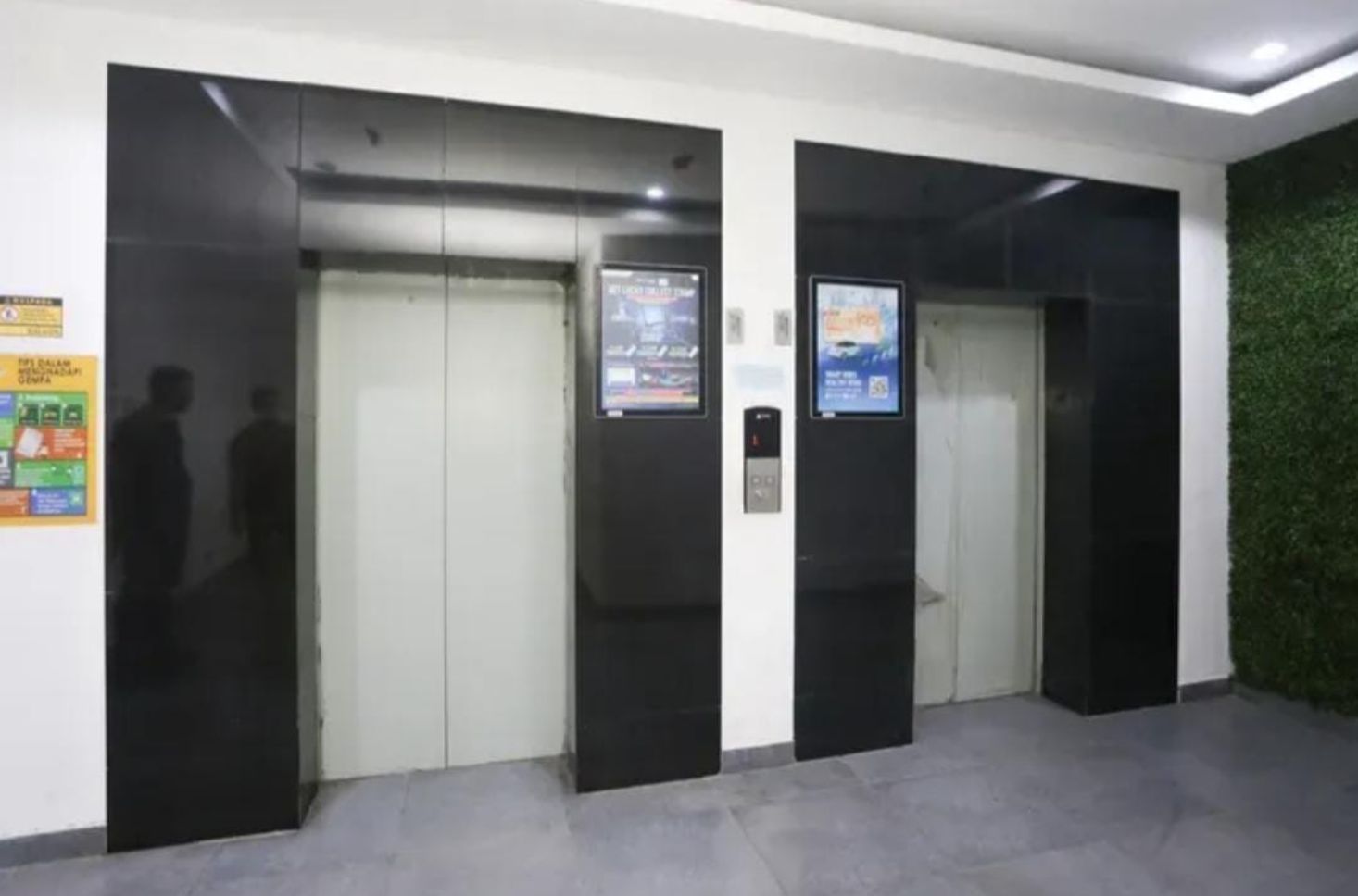 Conjunto de ascensores negros con pantallas digitales, una pared verde y un suelo de baldosas.