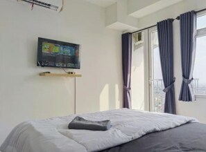 Habitación de hotel con cama, televisor montado en la pared y ventana con cortinas.