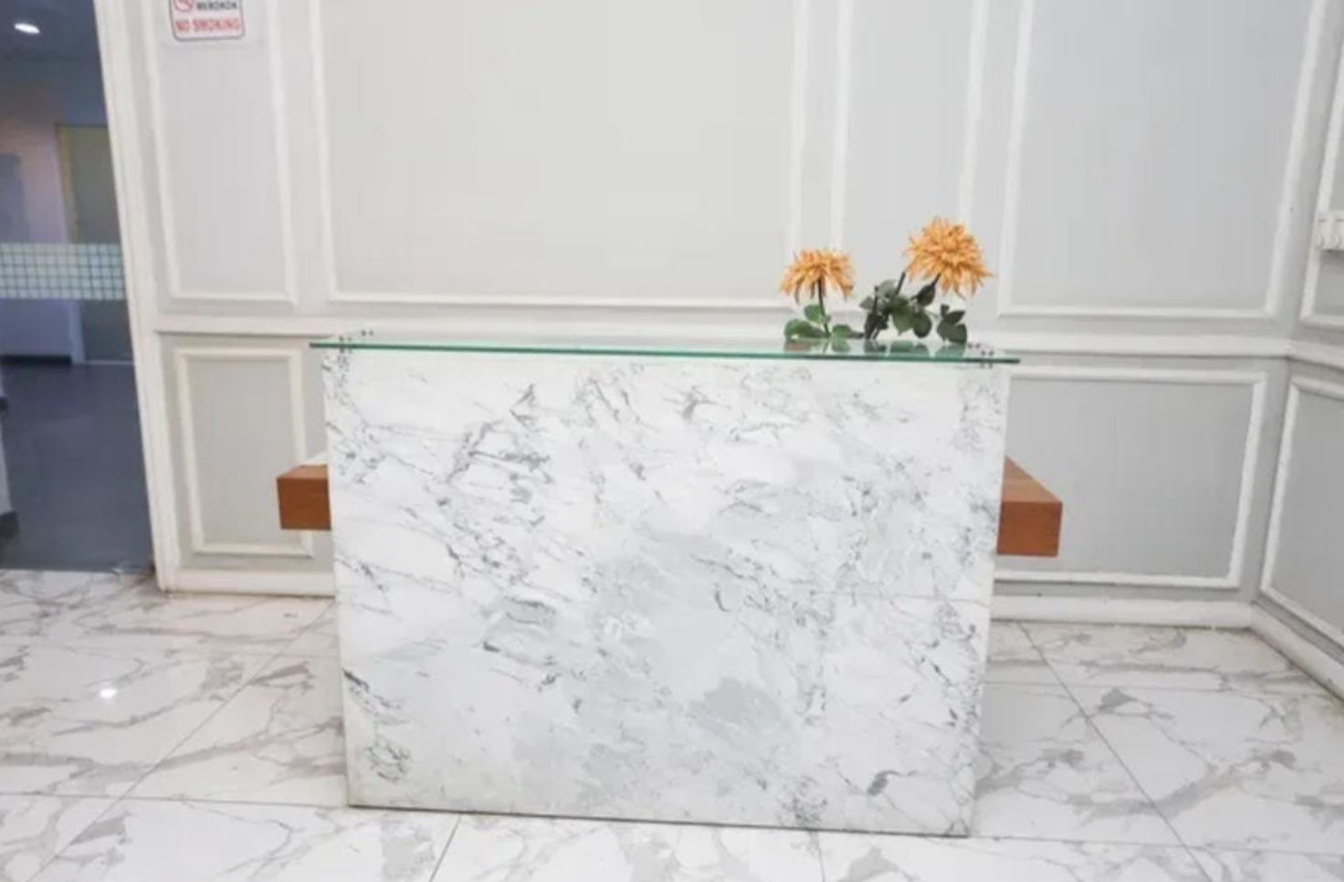 Una recepción con encimera de mármol, dos jarrones de flores y un letrero de 'No Fumar' en la pared.