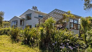 Una casa de dos pisos con un patio techado, rodeada de abundante vegetación y plantas en flor.
