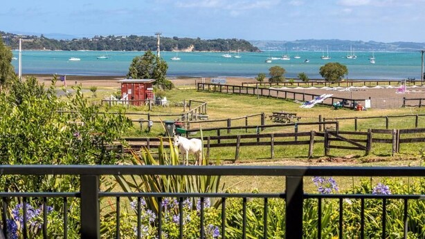 Vista costera con una zona cercada, un caballo blanco y barcos en el agua.