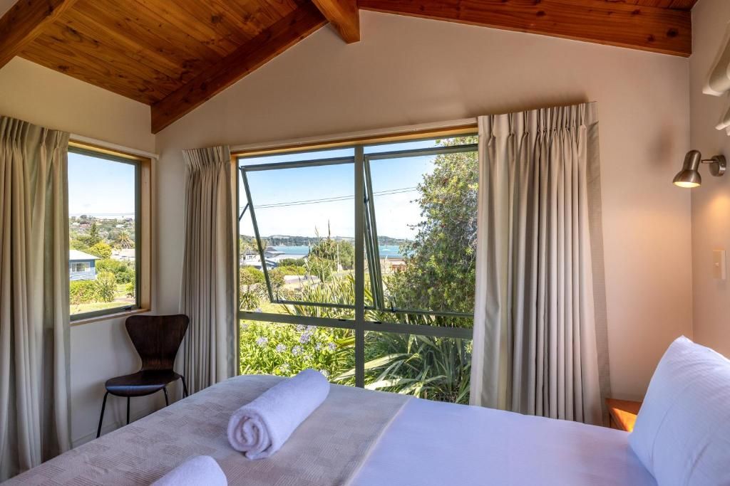 A hotel room with a bed, a chair, and large windows offering a view of the outdoors.