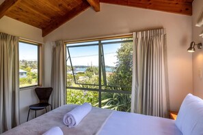A hotel room with a bed, a chair, and large windows offering a view of the outdoors.