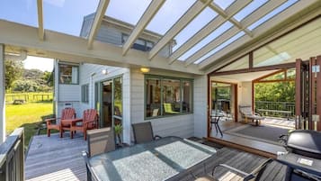A covered outdoor area with a table and chairs, a grill, and a view of a house and landscape.