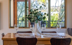 A dining table set with placemats, wine glasses, and cutlery, with a vase of greenery in the center.