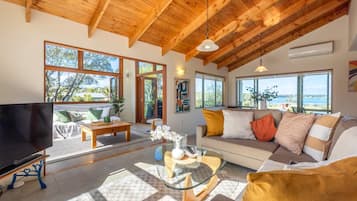 A spacious living room with a large TV, comfortable seating, and large windows offering a view of the outdoors.