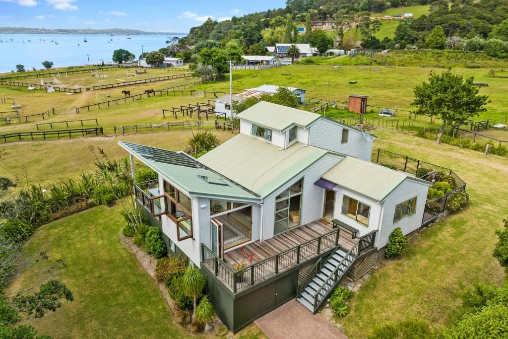 A two-story house with a balcony and a deck, surrounded by a fenced yard and a view of the sea.
