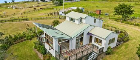 A two-story house with a balcony and a deck, surrounded by a fenced yard and a view of the sea.