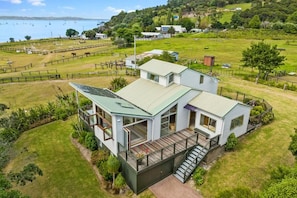 A two-story house with a balcony and a deck, surrounded by a fenced yard and a view of the sea.